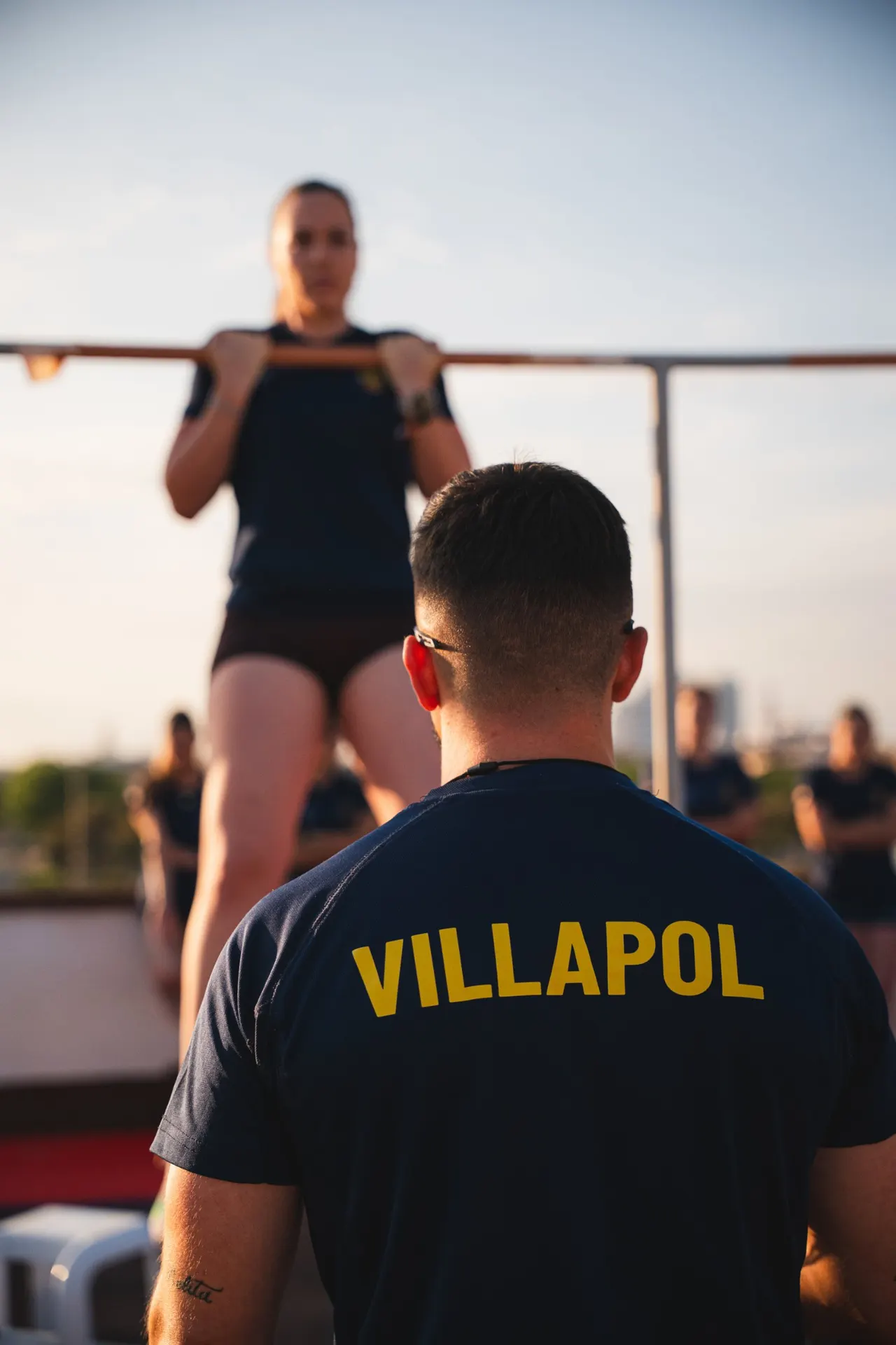Coach de Academia Villapol, de espaldas, junto a una alumna en la barra de dominadas
